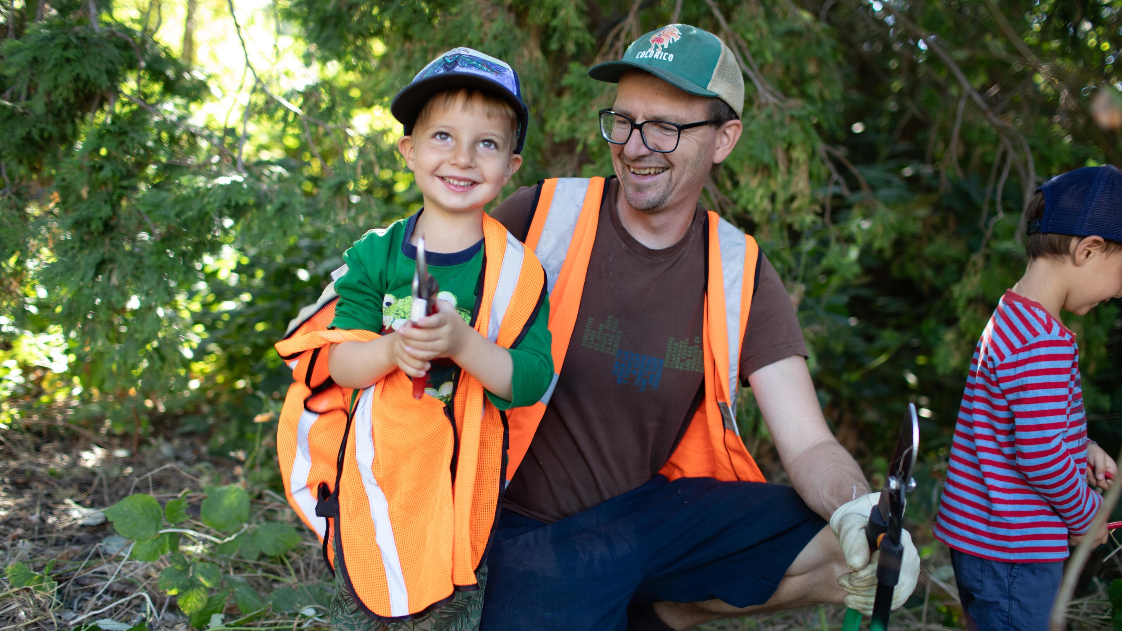 young boy and dad wearing orange vests and working on a park clean up