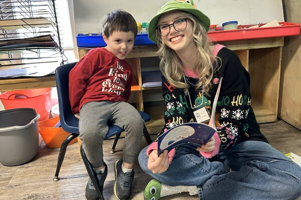 woman in a hat reading to a boy sitting in a chair