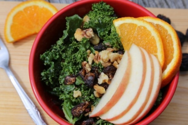 kale salad with apples and oranges in a red bowl