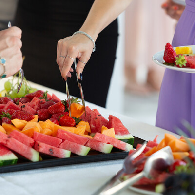fruit platter with hand using tongs to pick up a piece of watermelon