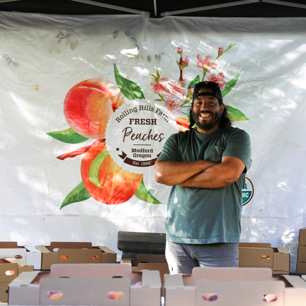 Produce Manager, Joe stands with arms crossed and smiling in his Peach Pop-Up Tent.