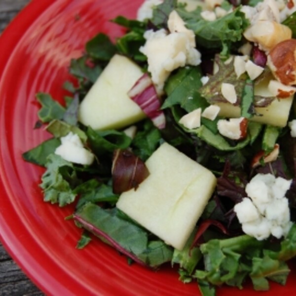 mixed green salad with honeycrisp apples hazelnuts and blue cheese on a red plate